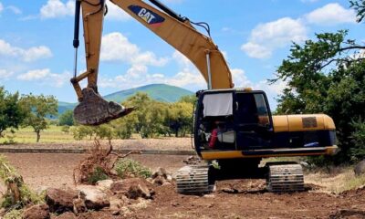 Excavadora trabajando en un camino rural de Huaquechula, removiendo piedras y maleza para rehabilitar brechas y facilitar el tránsito de campesinos tras las lluvias.