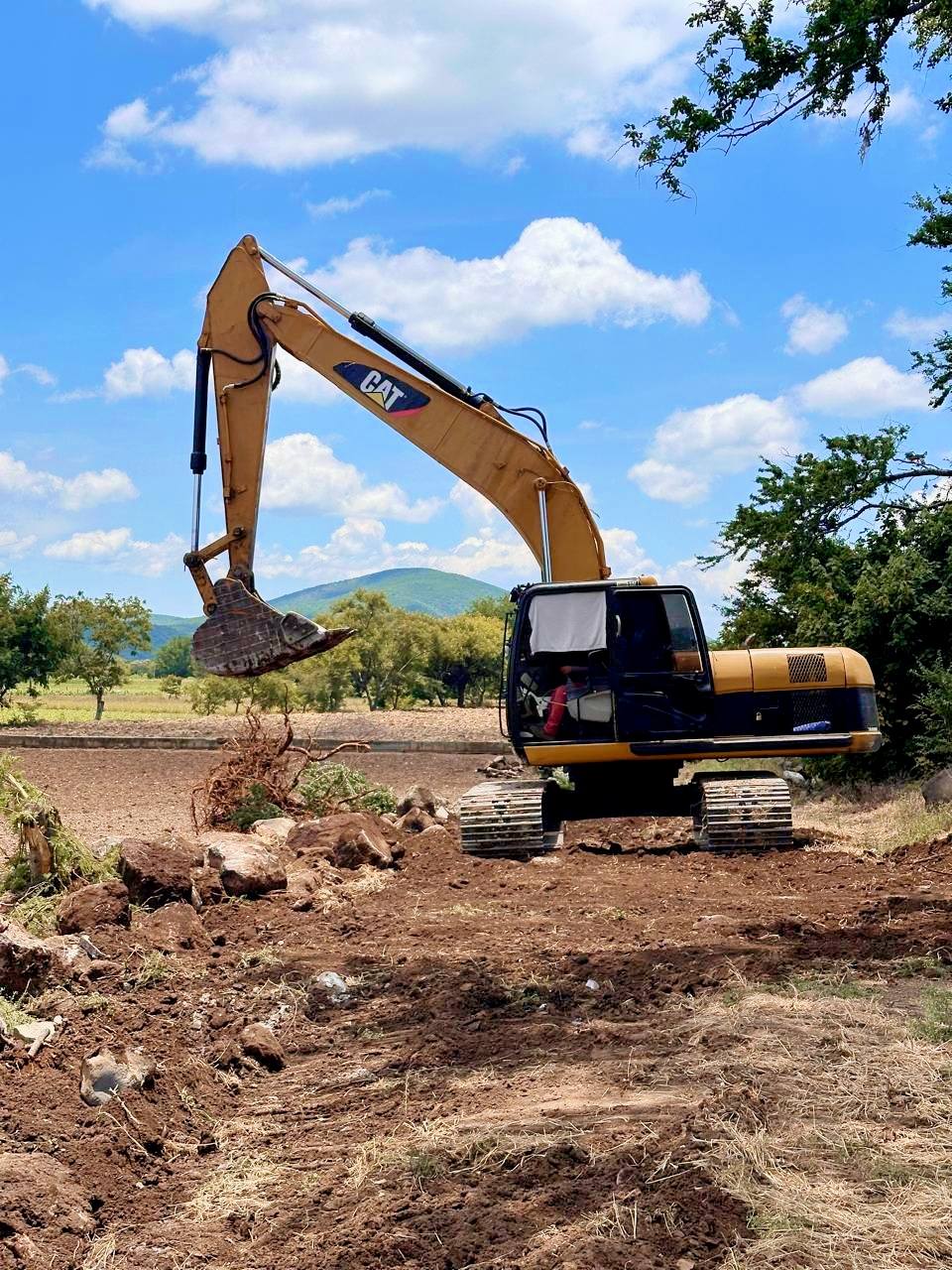 Excavadora trabajando en un camino rural de Huaquechula, removiendo piedras y maleza para rehabilitar brechas y facilitar el tránsito de campesinos tras las lluvias.