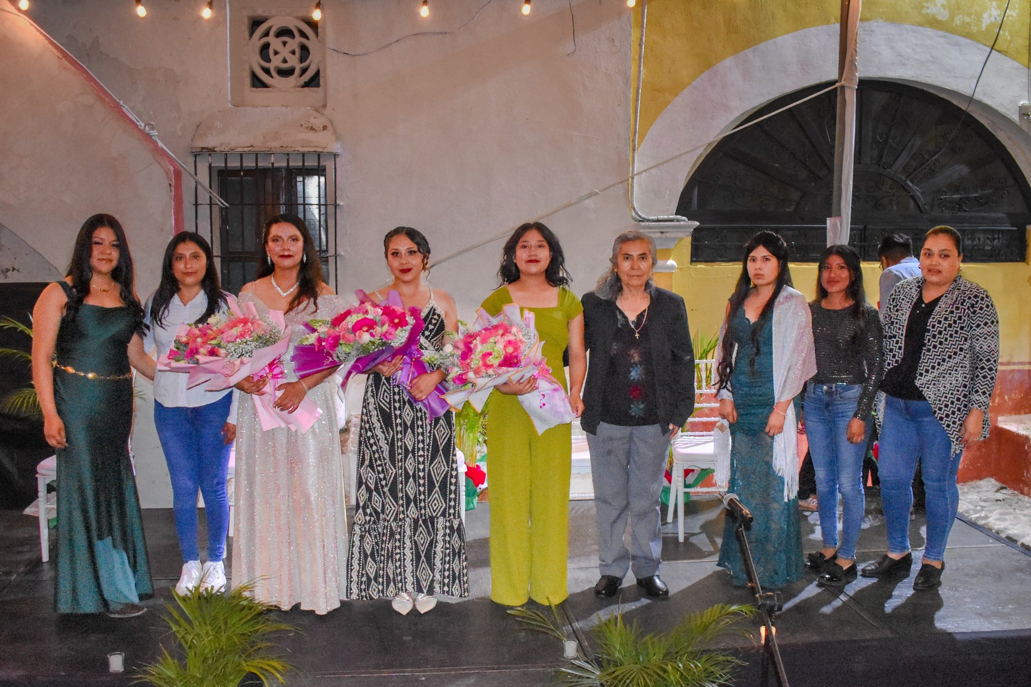 Grupo de mujeres en el escenario durante la coronación de la Reina y Princesas de las Fiestas Patrias 2025 en Huaquechula. Tres de ellas sostienen ramos de flores, destacando como representantes de la juventud y la tradición mexicana.