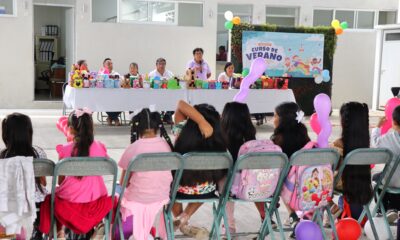 Niñas, niños y padres de familia participan en la clausura de los Cursos de Verano organizados por el DIF Municipal y el Ayuntamiento de Tochimilco. Se observa un grupo reunido en un espacio techado, con sillas, globos y actividades recreativas.