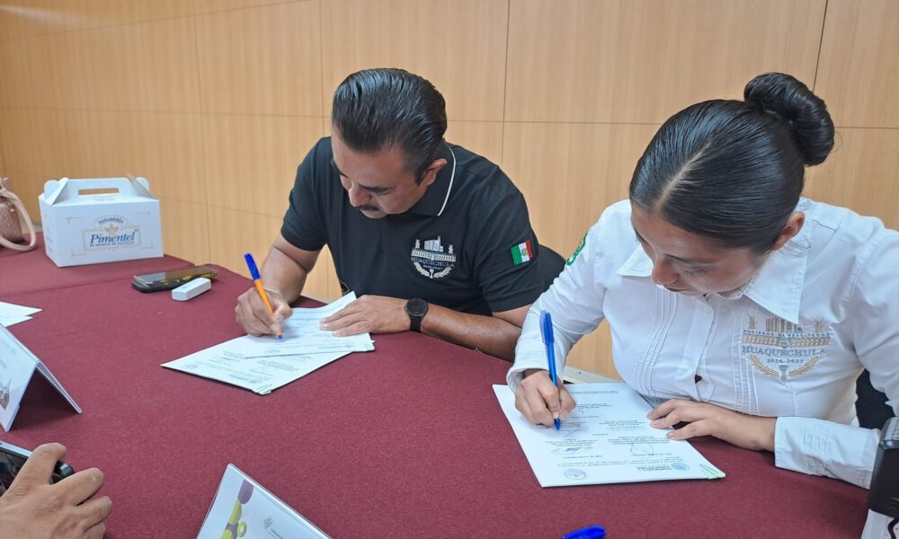 El presidente municipal de Huaquechula, Raúl Marín, y la Síndico Municipal firman un convenio de colaboración con el Poder Judicial del Estado de Puebla, en una mesa con documentos oficiales.