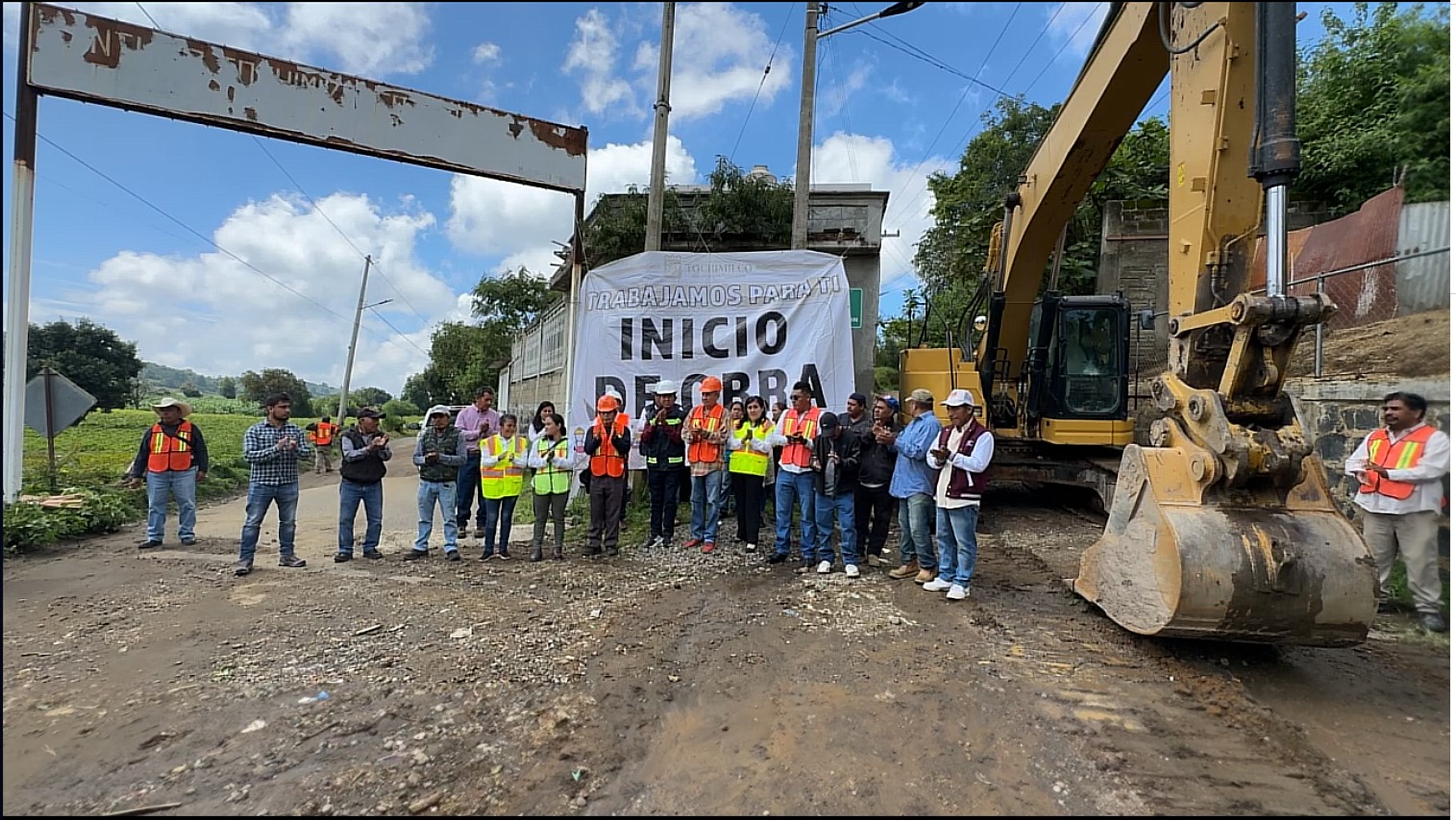 Grupo de autoridades municipales, vecinos y trabajadores de la construcción frente a una excavadora durante el banderazo de inicio de la pavimentación con concreto hidráulico en la calle Hombres Ilustres de Santiago Tochimizolco.
