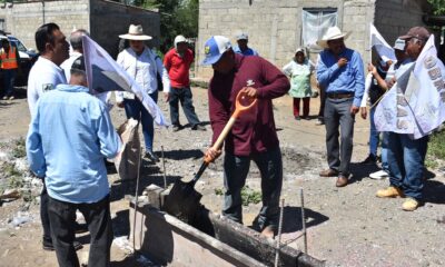 Un grupo de habitantes y autoridades municipales participa en el arranque de la obra de adoquinamiento en la calle Cuauhtémoc, en La Soledad Morelos, Huaquechula. Un hombre vierte mezcla de cemento con pala mientras la comunidad observa.