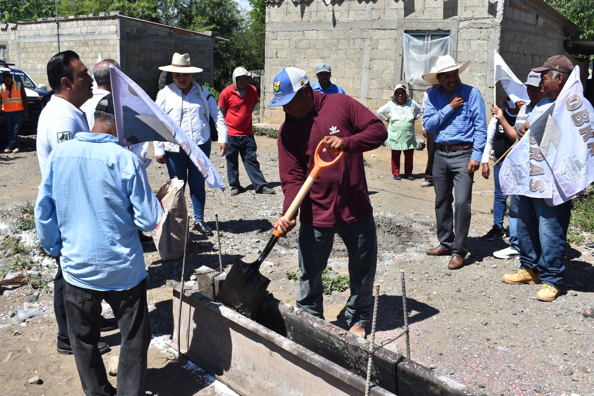 Un grupo de habitantes y autoridades municipales participa en el arranque de la obra de adoquinamiento en la calle Cuauhtémoc, en La Soledad Morelos, Huaquechula. Un hombre vierte mezcla de cemento con pala mientras la comunidad observa.