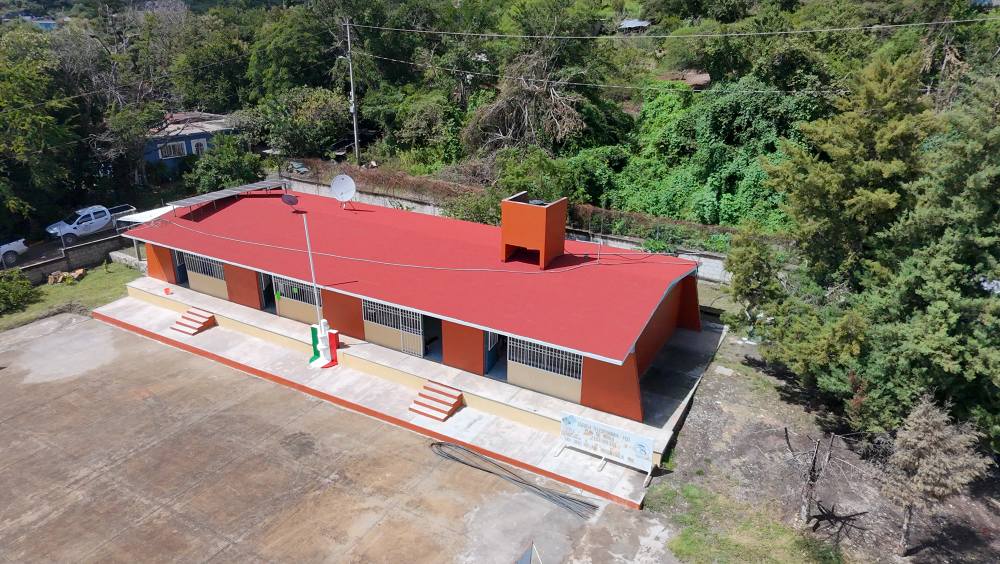 Vista aérea de la Telesecundaria “Plan de Ayala” en San Lucas Matlala, Huaquechula, tras su rehabilitación realizada por el ayuntamiento. El edificio muestra techado nuevo y fachada renovada, rodeado de vegetación.