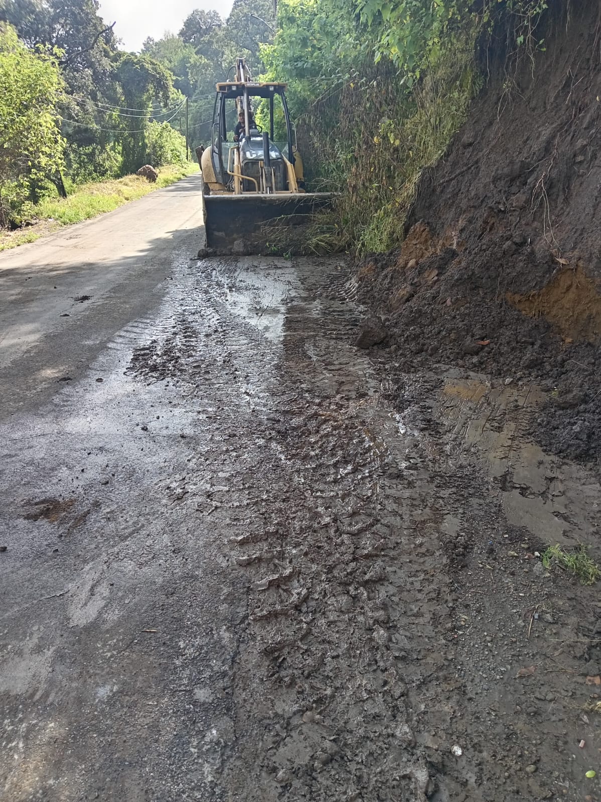 Maquinaria del Ayuntamiento de Tochimilco retira lodo y escombros tras un deslizamiento ocasionado por lluvias, con el objetivo de restablecer la circulación vehicular de manera segura.