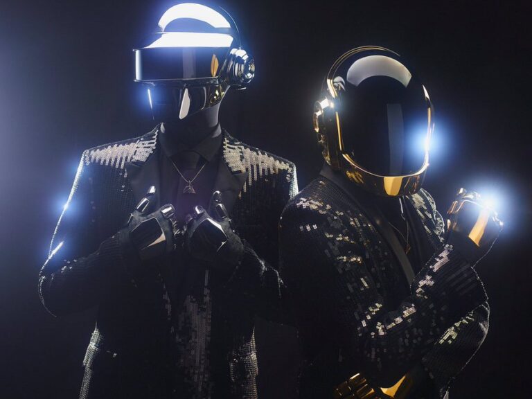 Dos integrantes de Daft Punk posan con sus icónicos cascos futuristas y trajes brillantes, símbolo de la música electrónica y la cultura digital.
