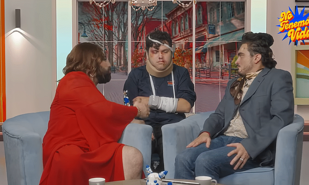 Tres comediantes caracterizados en un sketch satírico que parodia programas de espectáculos; uno de ellos aparece con vendajes y moretones, recreando un accidente ficticio.