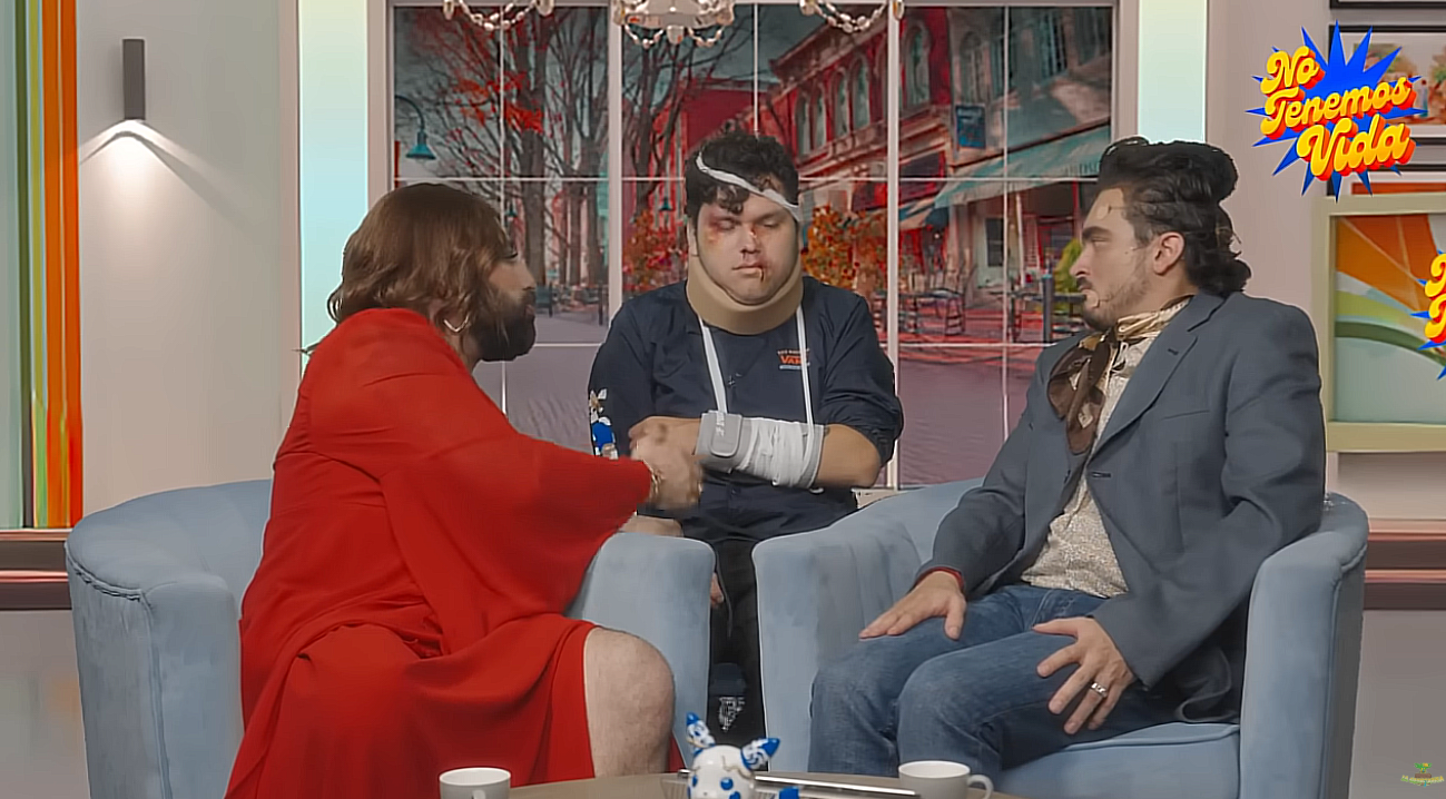 Tres comediantes caracterizados en un sketch satírico que parodia programas de espectáculos; uno de ellos aparece con vendajes y moretones, recreando un accidente ficticio.