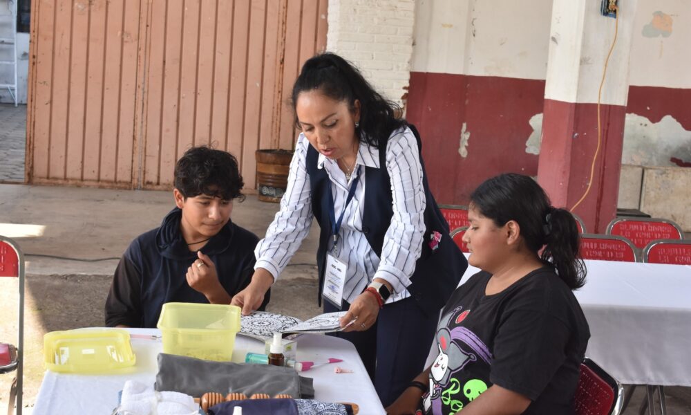 Una instructora de la Misión Cultural #15 en Cacaloxuchitl guía a jóvenes durante un taller práctico de manualidades, promoviendo el aprendizaje y la capacitación comunitaria.