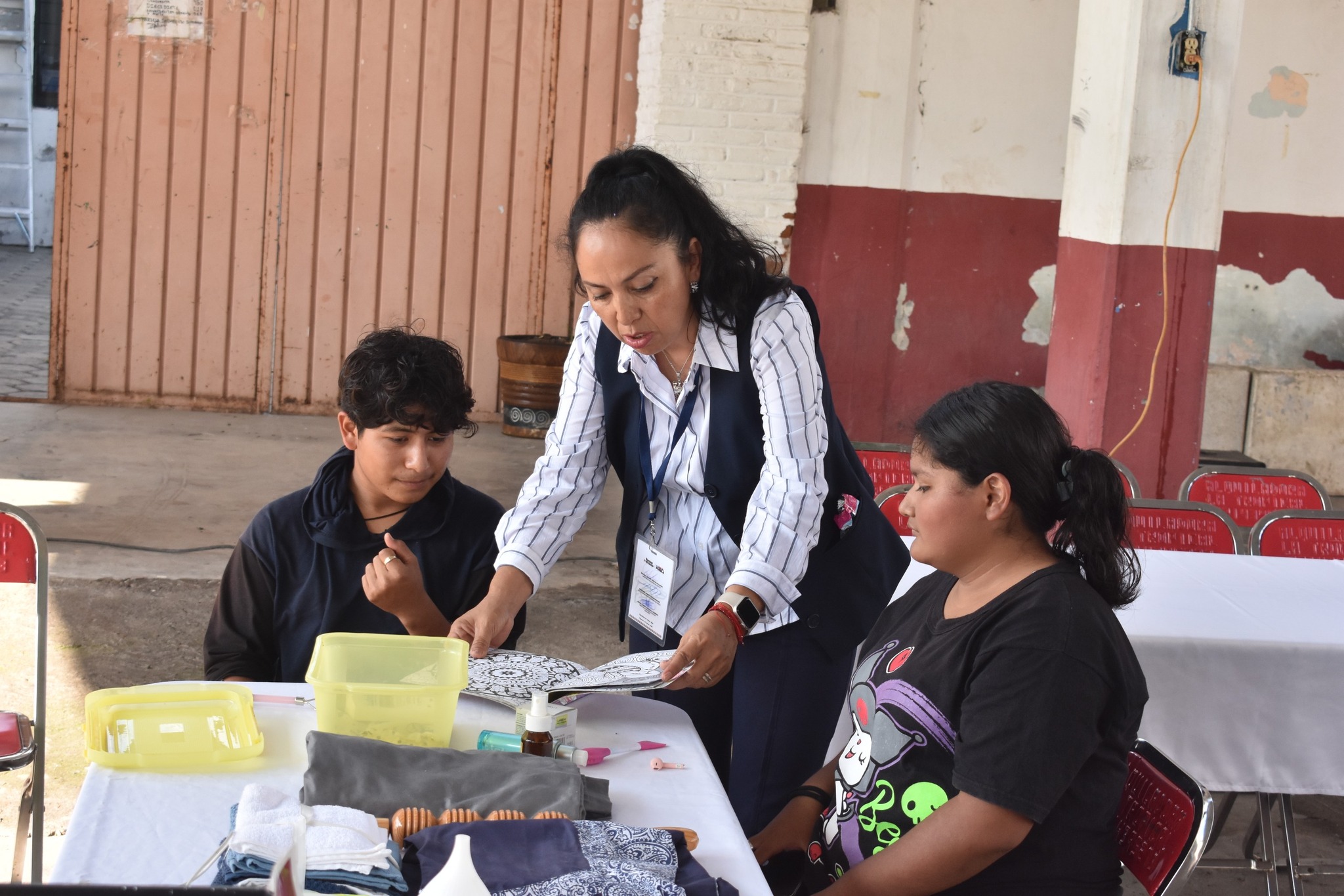 Una instructora de la Misión Cultural #15 en Cacaloxuchitl guía a jóvenes durante un taller práctico de manualidades, promoviendo el aprendizaje y la capacitación comunitaria.