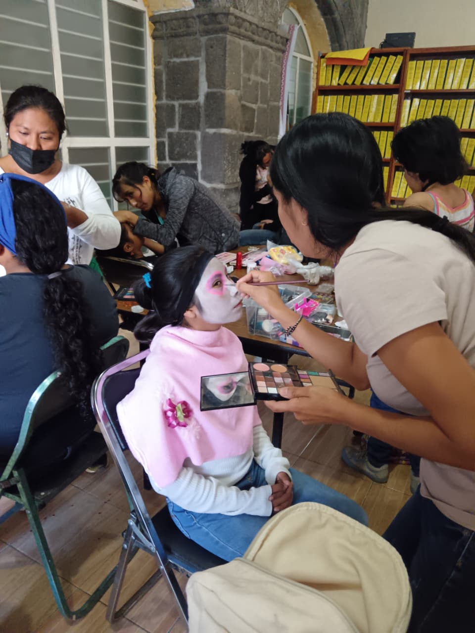 Mujer maquillando a niña en el Taller de Autoempleo de Maquillaje Artístico del DIF Municipal Tochimilco, con temática del Día de Muertos.