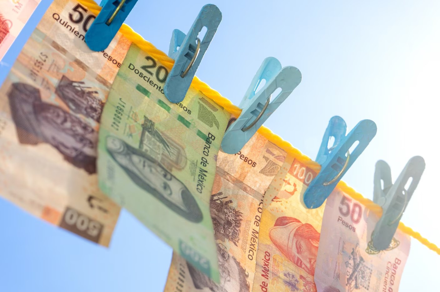 Fotografía de billetes mexicanos colgados con pinzas en un tendedero, representando las nuevas familias de billetes emitidas por el Banco de México.
