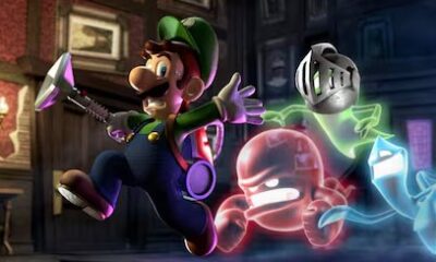Luigi corriendo con su aspiradora cazafantasmas mientras tres fantasmas coloridos lo persiguen dentro de una mansión oscura en Luigi’s Mansion.