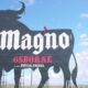Persona subiendo al icónico anuncio metálico del toro de Magno Osborne, clásico emblema publicitario visible en carreteras.