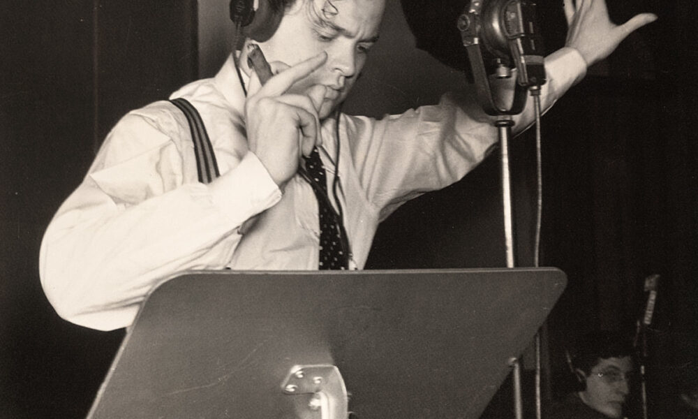 Fotografía histórica en blanco y negro de un hombre con auriculares y micrófono durante una transmisión de radio en vivo.