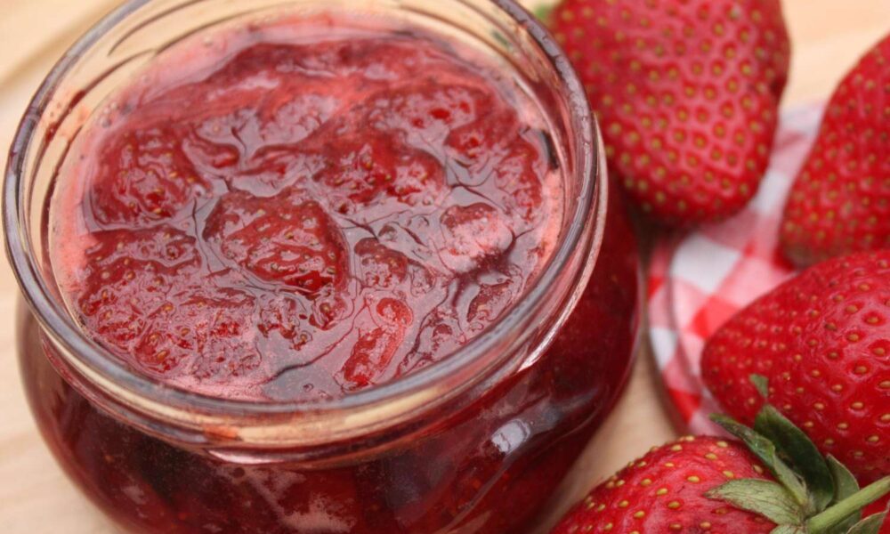 Frasco de mermelada de fresa artesanal acompañado de fresas frescas sobre una mesa de madera, representando la preparación casera y natural promovida por el taller organizado en Huaquechula.