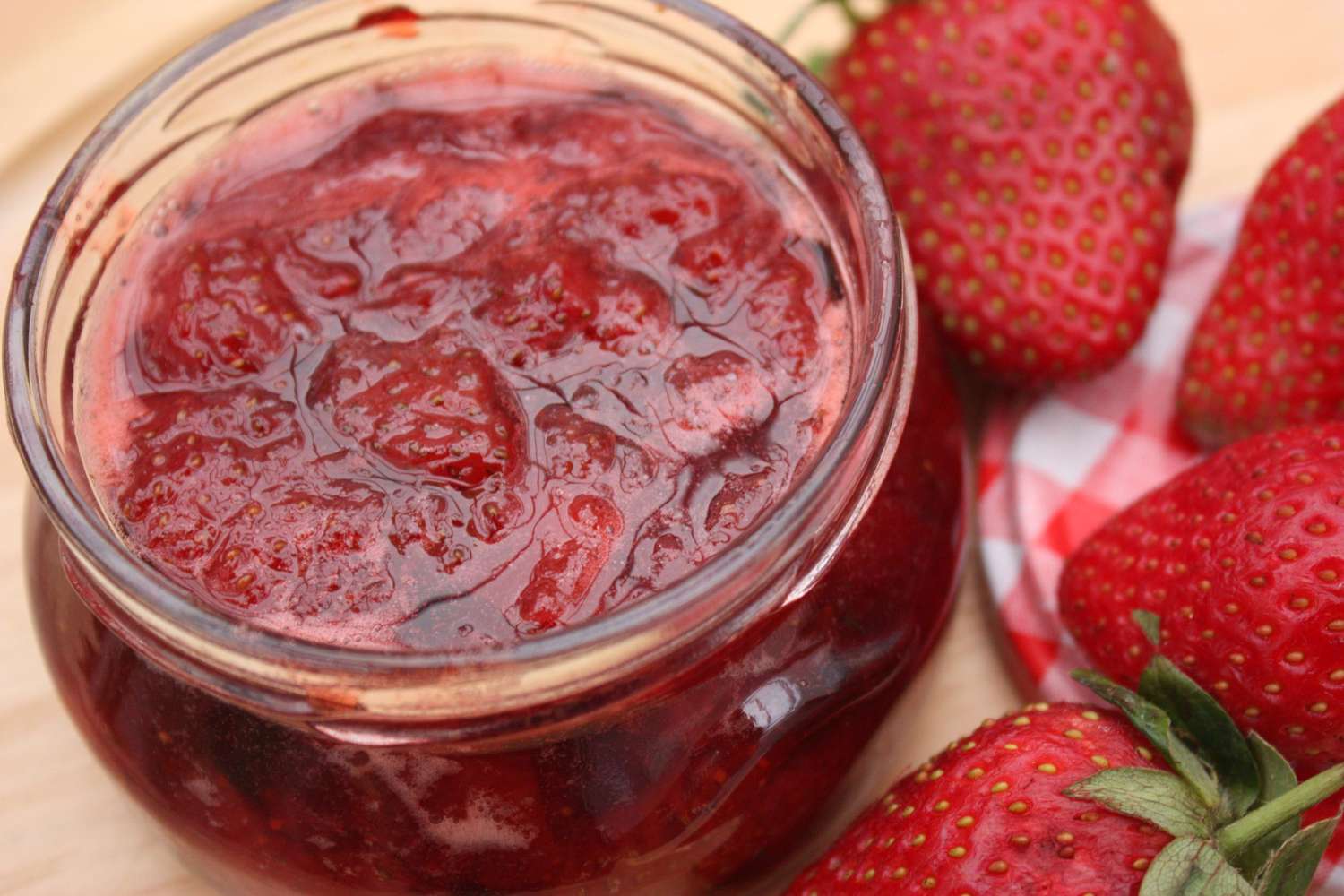 Frasco de mermelada de fresa artesanal acompañado de fresas frescas sobre una mesa de madera, representando la preparación casera y natural promovida por el taller organizado en Huaquechula.
