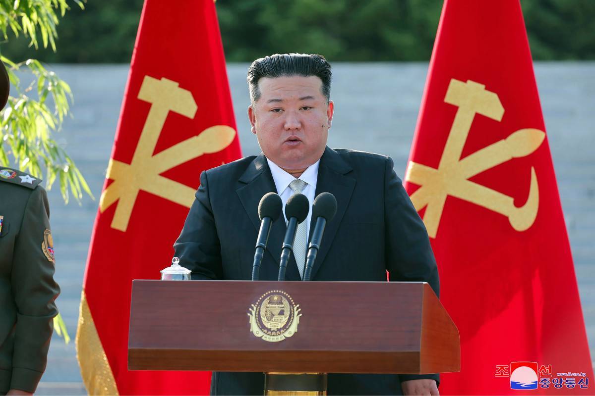 Líder norcoreano hablando en un podio con micrófonos y banderas oficiales detrás, en un evento político.