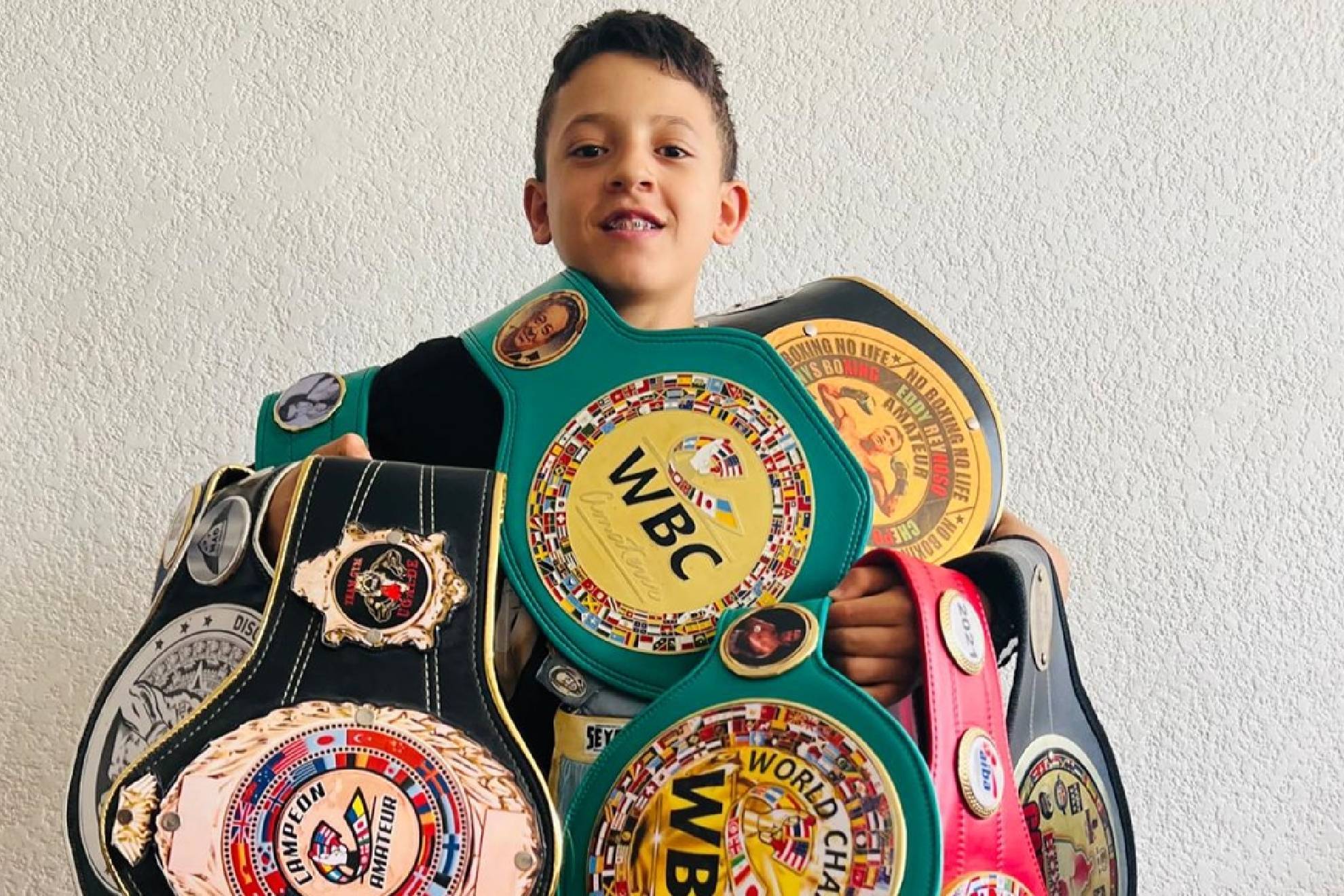 Joven boxeador mexicano sosteniendo múltiples cinturones de campeón tras debut profesional a los 16 años.