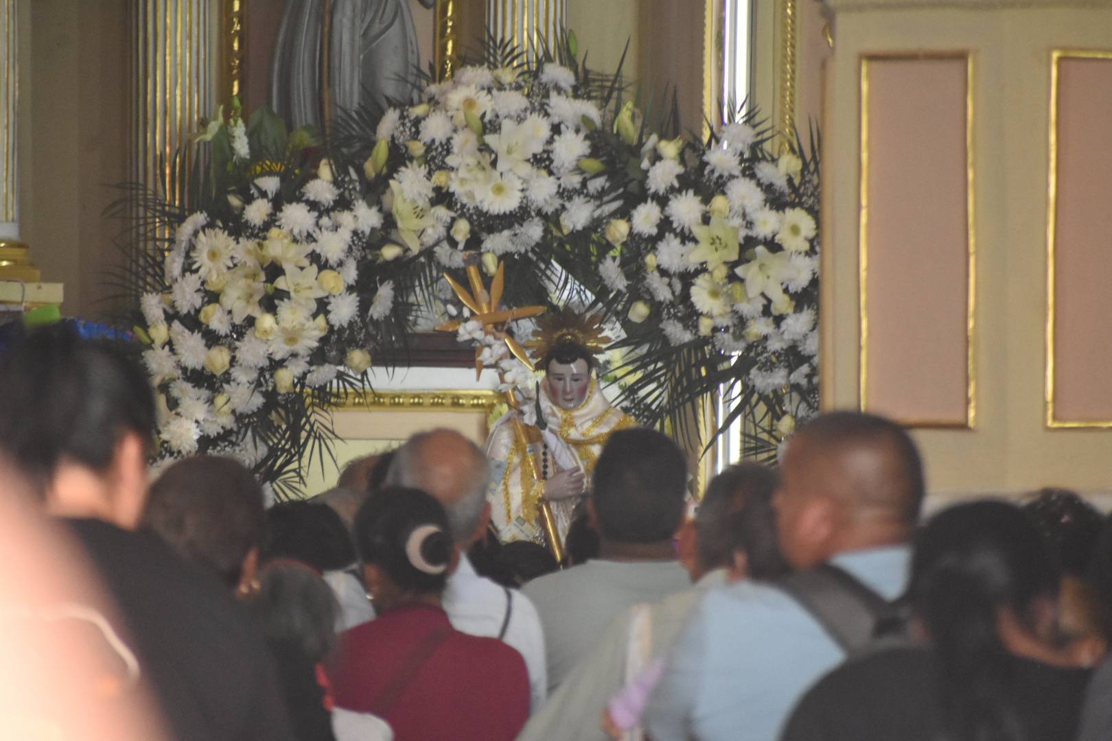 Imagen de la figura de San Diego de Alcalá adornada con flores durante la fiesta patronal en San Juan Huiluco, rodeada de asistentes dentro del templo.