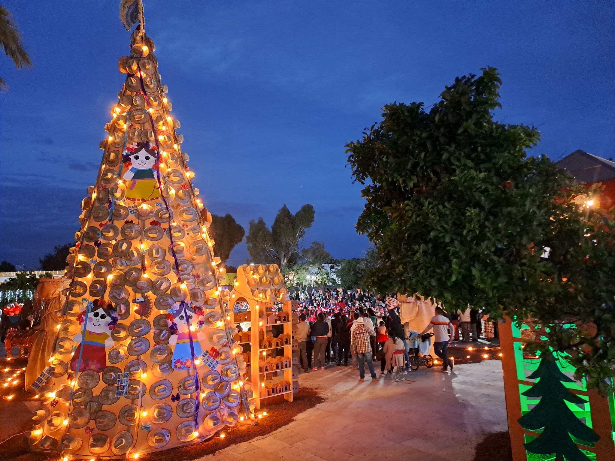 Nacimiento Monumental Artesanal iluminado por la noche, construido con materiales tradicionales en la cabecera municipal de Huaquechula, con visitantes reunidos alrededor.