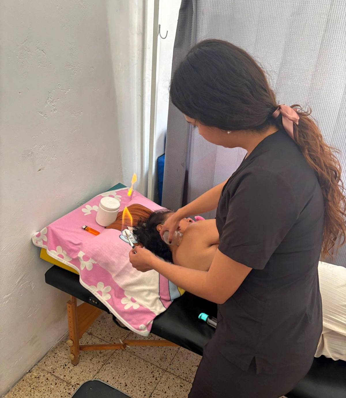 Profesional de fisioterapia aplicando terapia con ventosas a una paciente recostada sobre una camilla en una sala de rehabilitación.