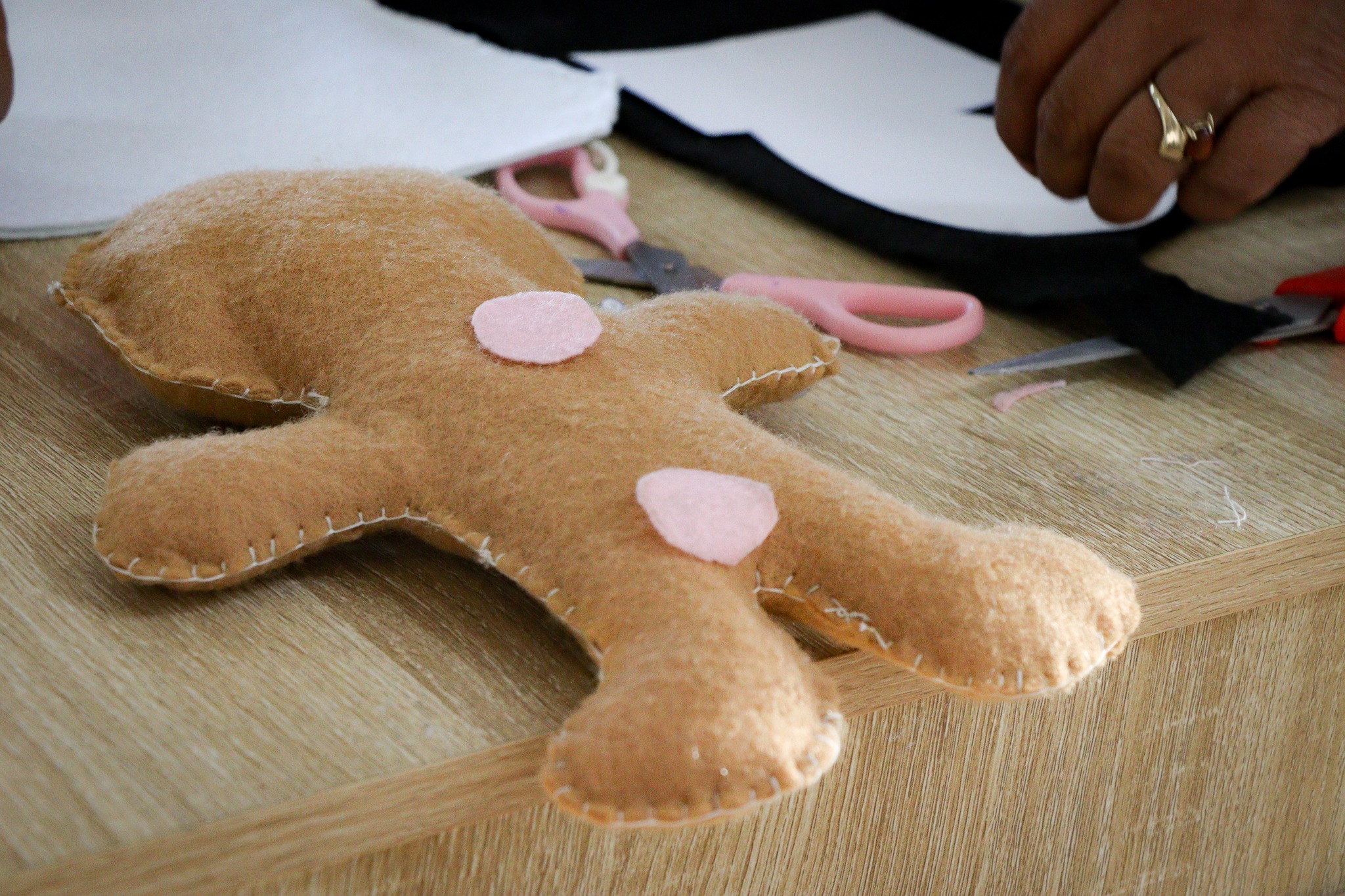 Figura artesanal de fieltro en proceso de elaboración, con tijeras y materiales de costura sobre una mesa durante un taller creativo comunitario.