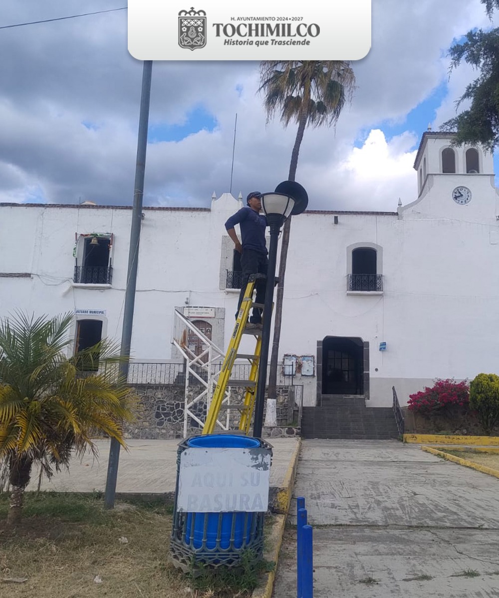 Trabajador de servicios públicos en una escalera dando mantenimiento a una luminaria en la cabecera municipal de Tochimilco, frente a la presidencia municipal.
