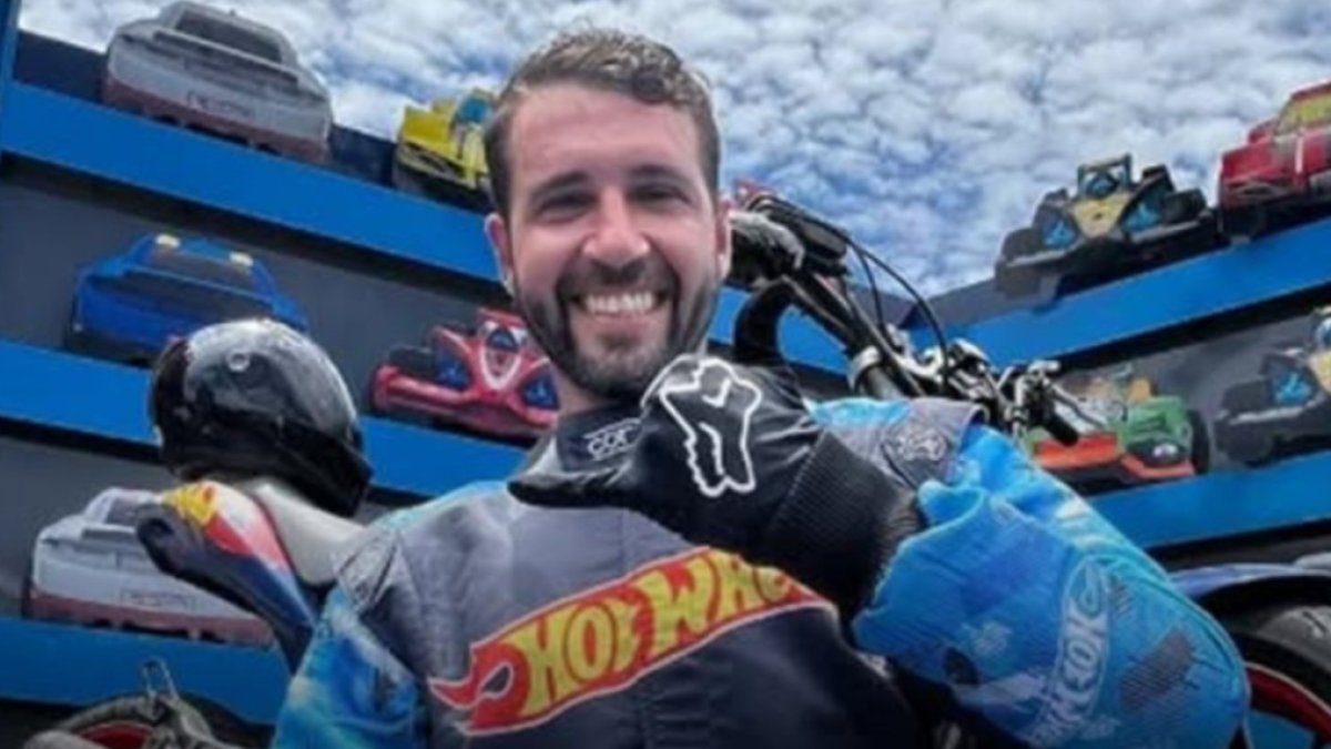 Piloto profesional vestido con traje de Hot Wheels sonriendo antes de realizar acrobacias en motocicleta.