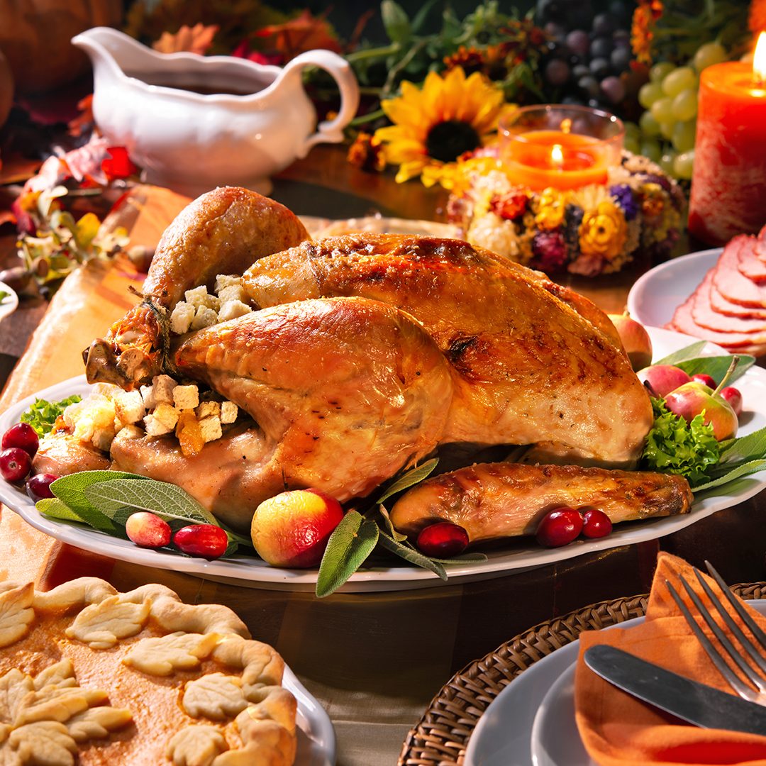Persona sirviendo pavo en una mesa con velas durante una cena de Thanksgiving o Acción de Gracias.