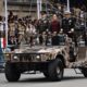 Vehículo militar con autoridades nacionales participando en desfile público frente a asistentes y banderas de México.