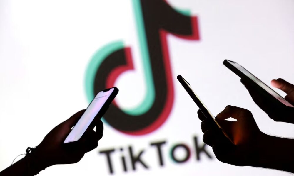 Tres personas sostienen teléfonos inteligentes frente al logo de TikTok, en un ambiente oscuro que resalta el uso constante de la plataforma.