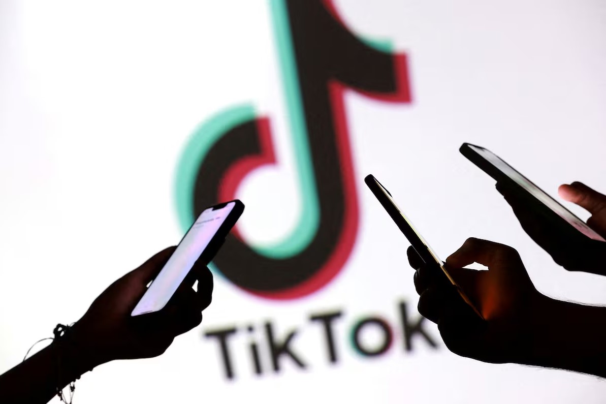Tres personas sostienen teléfonos inteligentes frente al logo de TikTok, en un ambiente oscuro que resalta el uso constante de la plataforma.