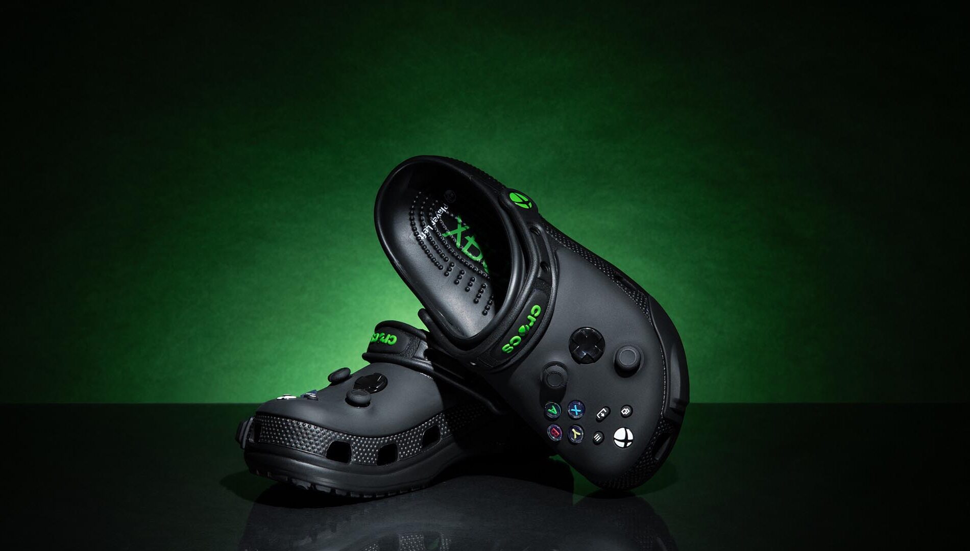 Crocs color negro edición especial inspirados en Xbox, con botones y diseño similar al control de la consola, sobre fondo verde oscuro.
