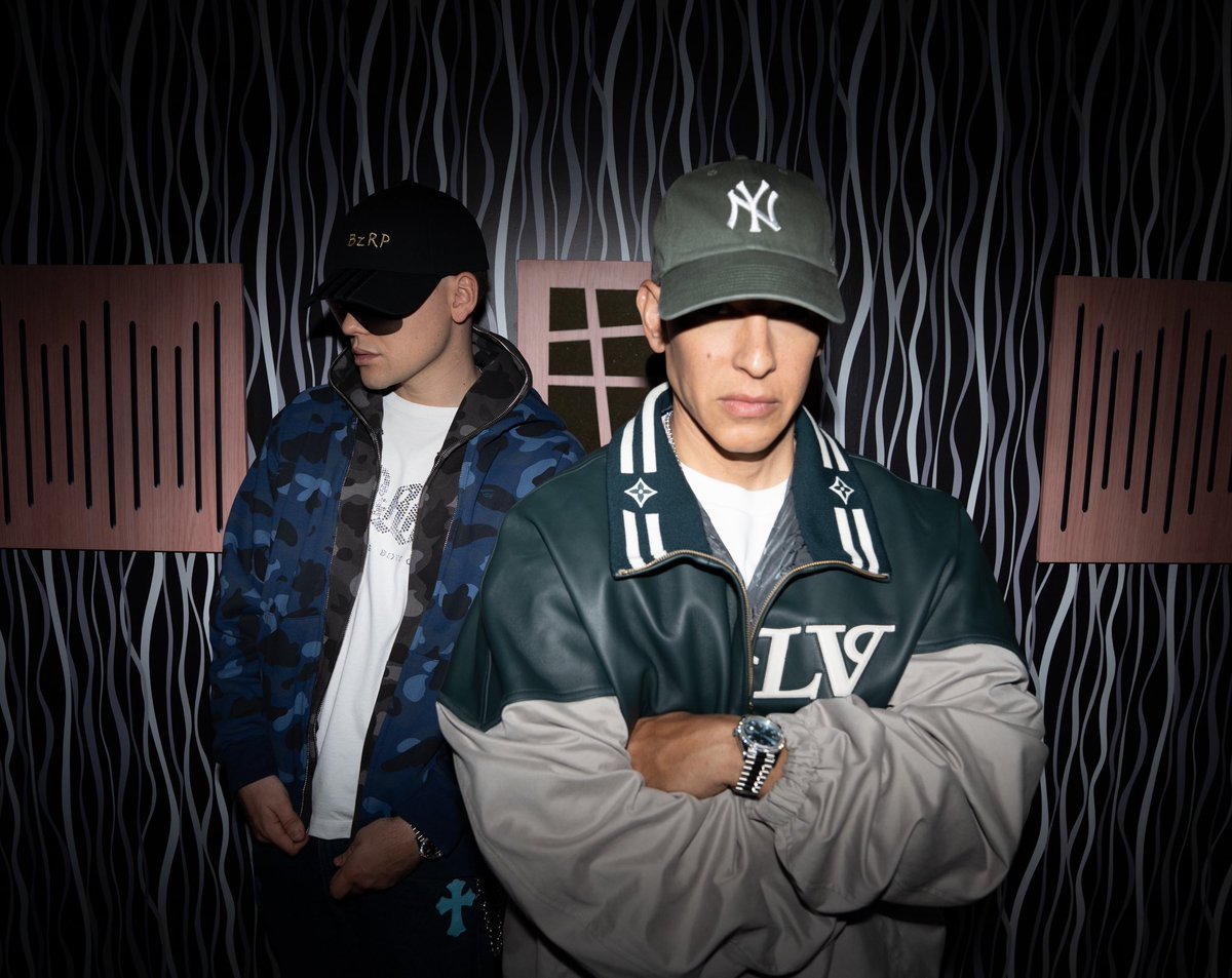 Bizarrap y Daddy Yankee posan en un estudio de grabación, vestidos con chamarras deportivas y gorras, antes del estreno de su nueva colaboración musical.