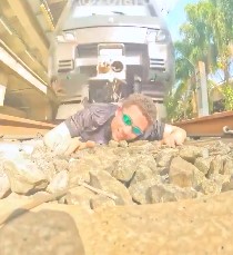 Persona recostada en rieles mientras un tren pasa encima, grabando el momento.