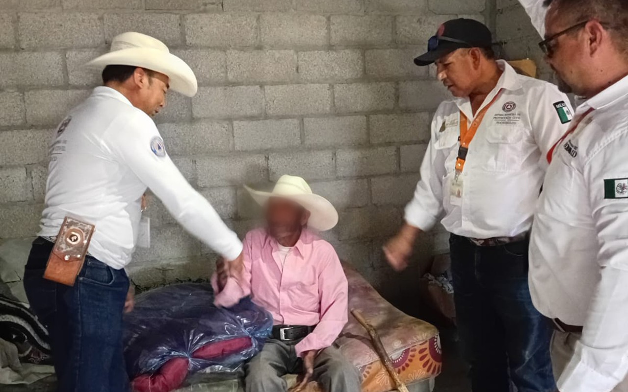 Personal de Protección Civil de Tochimilco entrega cobijas y colchonetas a un adulto mayor en situación vulnerable dentro de su vivienda.