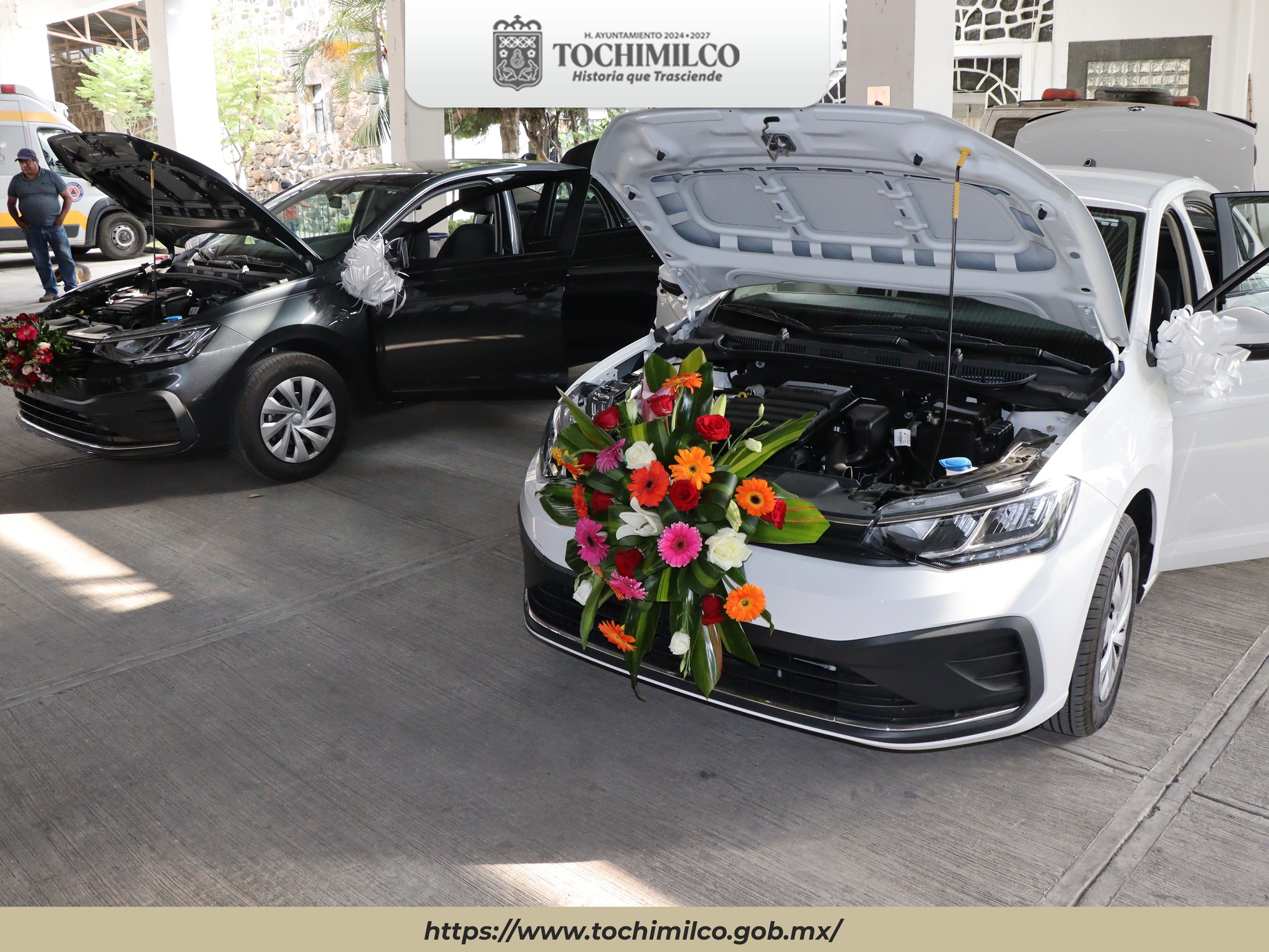 Dos automóviles nuevos con arreglos florales y cofre abierto durante su entrega oficial al DIF Municipal en Tochimilco.