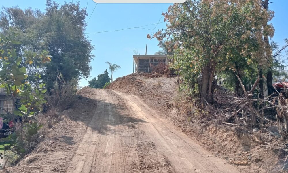 Camino de tierra en proceso de ampliación y nivelación en la colonia El Progreso, San Antonio Alpanocan, con dos personas observando el avance al fondo.