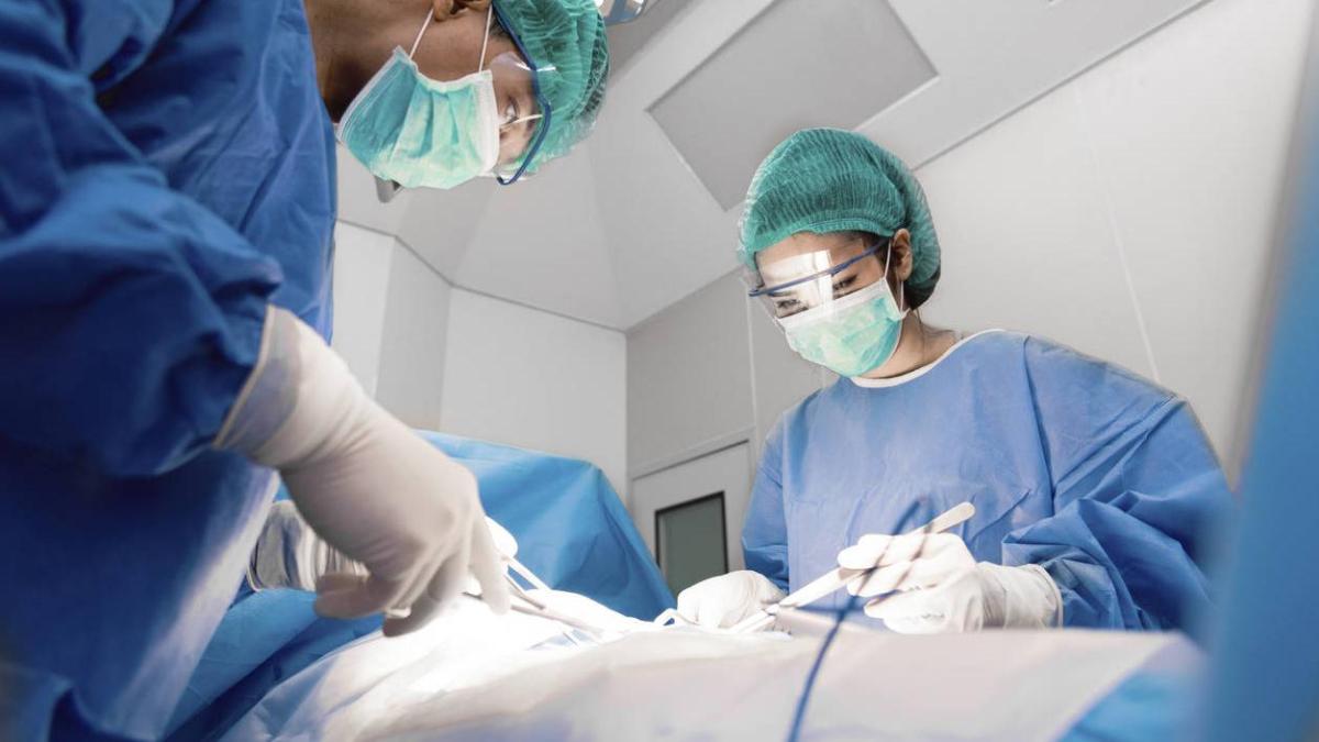 Equipo quirúrgico realizando una operación en un quirófano con tecnología médica y personal con bata, guantes y cubrebocas.