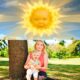 Montaje con el antiguo sol de un programa infantil con cara de bebé en el cielo y, debajo, una mujer joven sentada en el pasto abrazando a su hija pequeña en un parque.