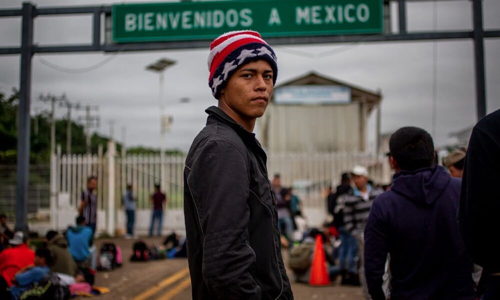 Persona migrante frente a un letrero de “Bienvenidos a México” en un cruce fronterizo.