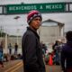 Persona migrante frente a un letrero de “Bienvenidos a México” en un cruce fronterizo.