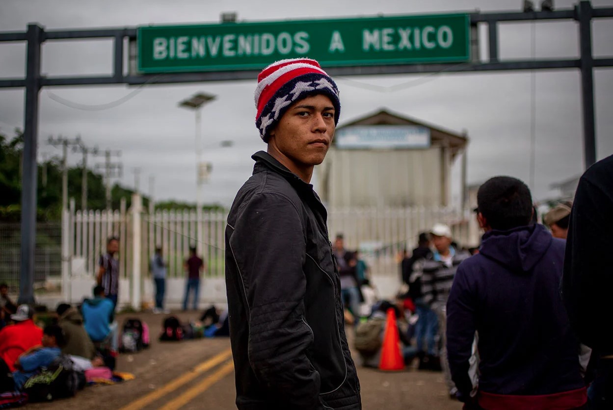 Persona migrante frente a un letrero de “Bienvenidos a México” en un cruce fronterizo.