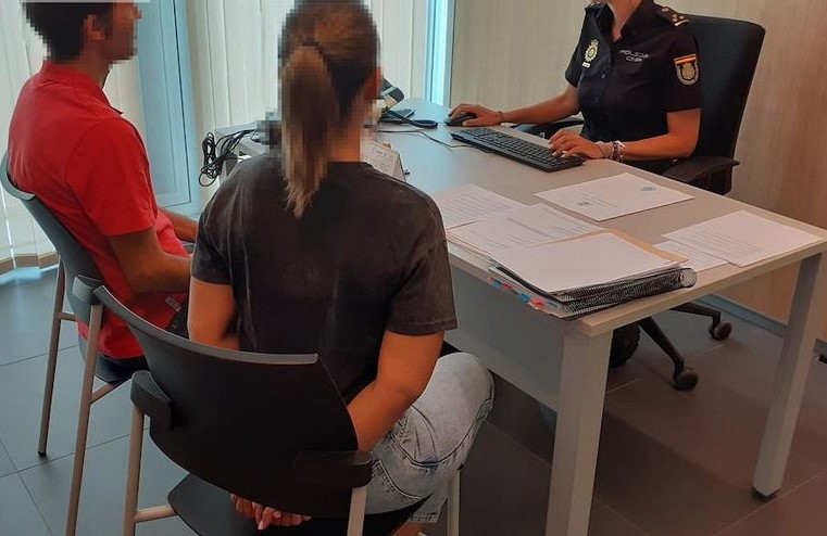 Pareja sentada frente a una oficial en una oficina realizando un trámite o proceso legal, conversando sobre documentos judiciales.