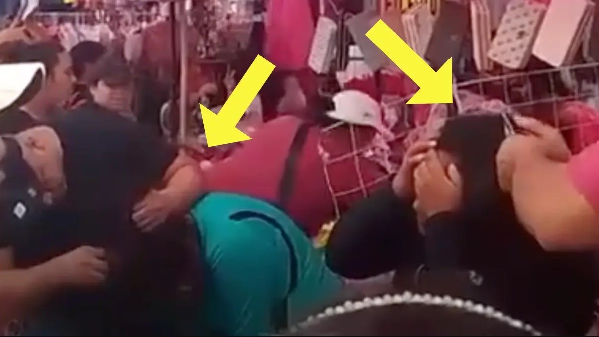 Comerciantes someten a dos mujeres acusadas de robo en un mercado, mientras varias personas observan y señalan la escena.