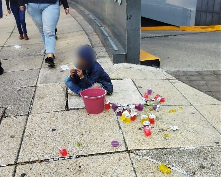 Menor sentado en la banqueta de una avenida de la Ciudad de México con un bote de gelatinas para venta.