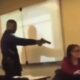 Estudiante amenaza a docente con un arma dentro de un salón de clases mientras otros observan.
