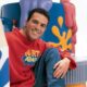 Presentador Rui Torres de Art Attack sonriendo en un set colorido con lápices gigantes.